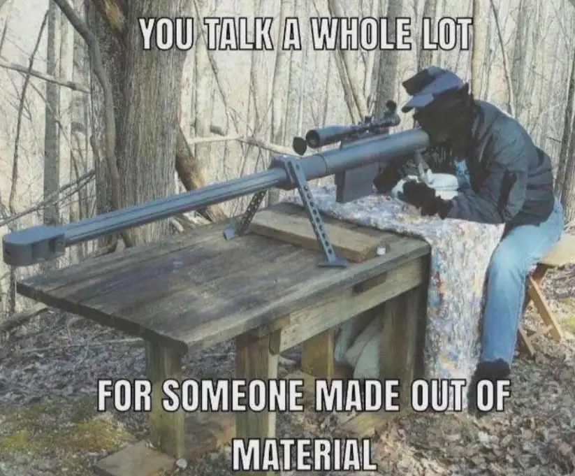 A person wearing a cap and dark clothing is seated at a wooden table outdoors in a wooded area, aiming a large…