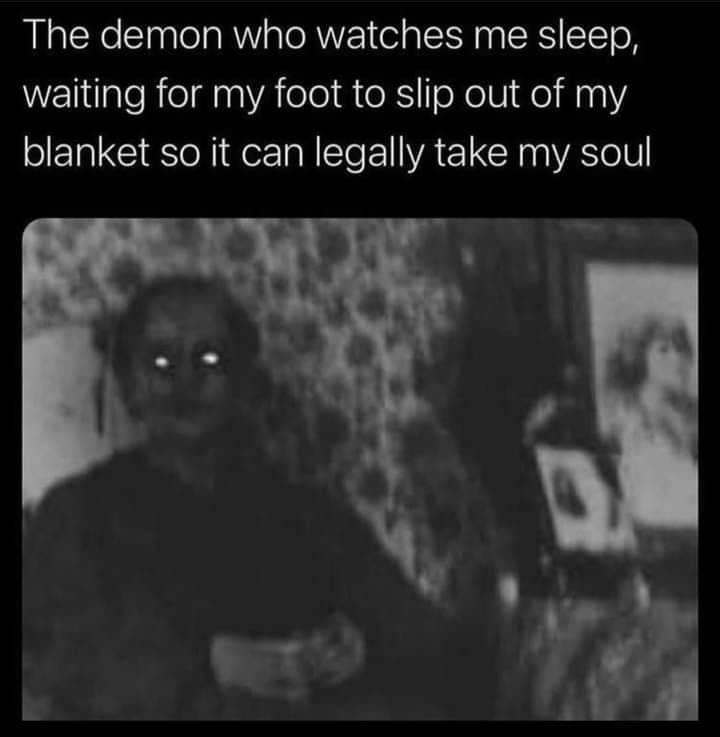 A grainy black-and-white image shows a blurry, unsettling figure with glowing eyes sitting in a dimly lit room with…
