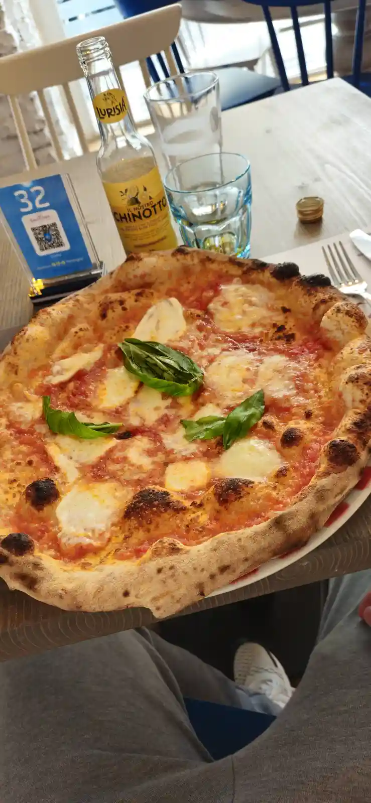 A close-up photo shows a freshly baked, rustic-style pizza with tomato sauce, melted mozzarella cheese, and fresh basil…