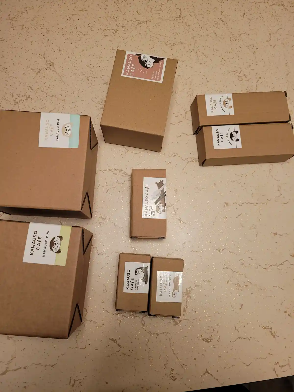 Several brown cardboard boxes from 'Kawauso Cafe' are arranged on a speckled countertop, each labeled with a cute otter…