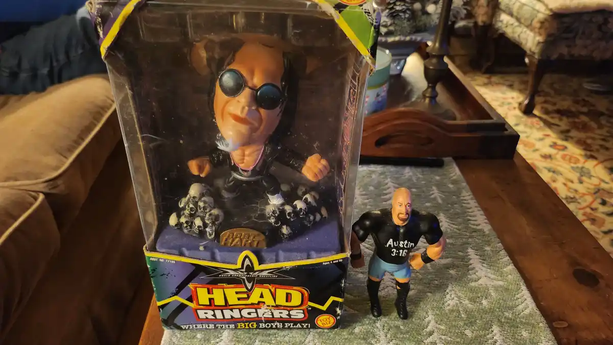 A vintage 'Head Ringers' wrestling toy box featuring a large, exaggerated head of Bret Hart with sunglasses and skulls, sits…