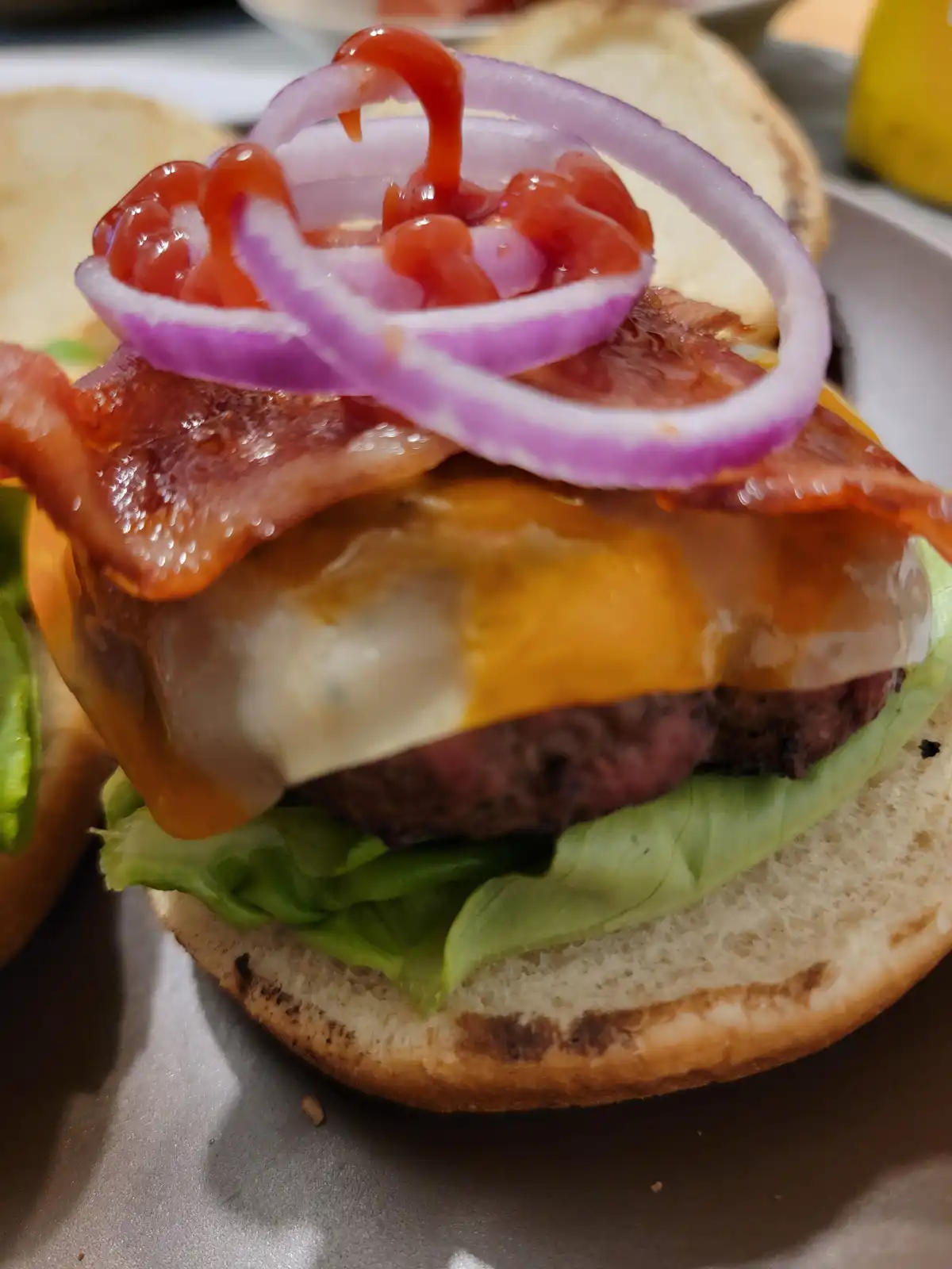 A close-up photo of a gourmet burger with a beef patty, melted cheese, crispy bacon, fresh lettuce, and red onion rings…