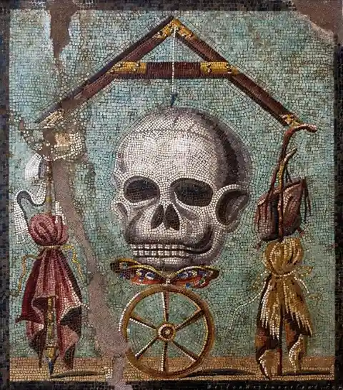 An ancient mosaic depicts a human skull hanging from a gallows-like structure, flanked by two figures in elaborate costumes…