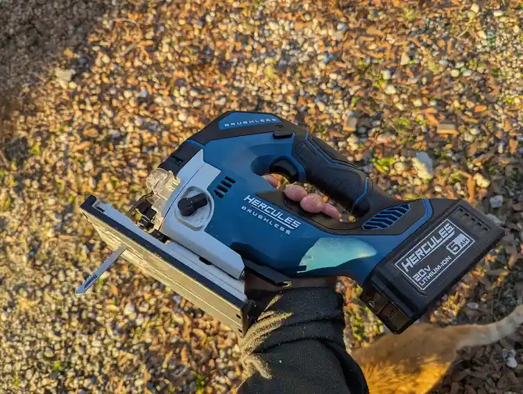 A hand holds a blue and black DeWalt Hercules brushless jigsaw with a 20V lithium-ion 5Ah battery pack, standing on a…