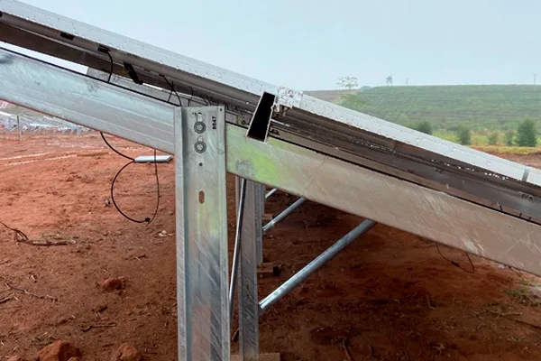A close-up photo of solar panels mounted on a metal frame in a dirt field, showing a visible gap where the panels are not…
