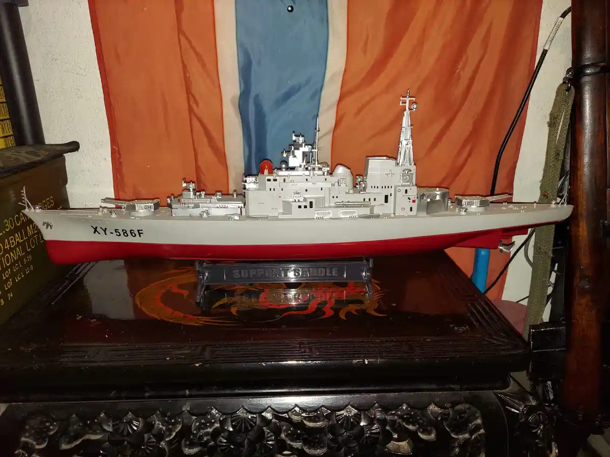 A detailed model of a grey and red naval ship with the hull number XY-586F is displayed on a black stand labeled 'SUPPORT…