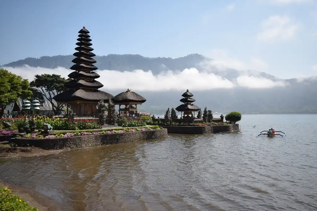A scenic photo of the Ulun Danu Bratan Temple in Bali, Indonesia, with traditional tiered roofs, surrounded by water and…