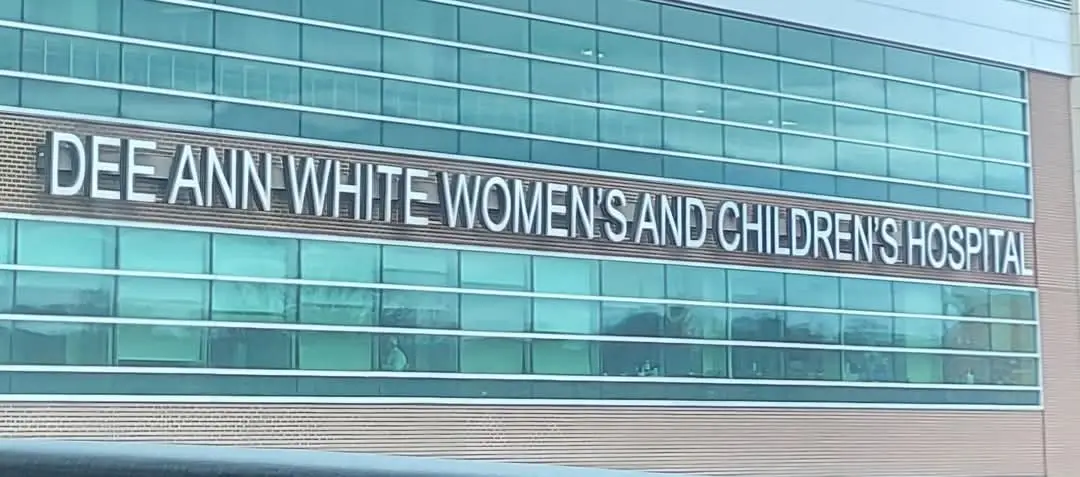 A photo of a modern hospital building with large glass windows and a brick facade. A prominent sign on the building reads…