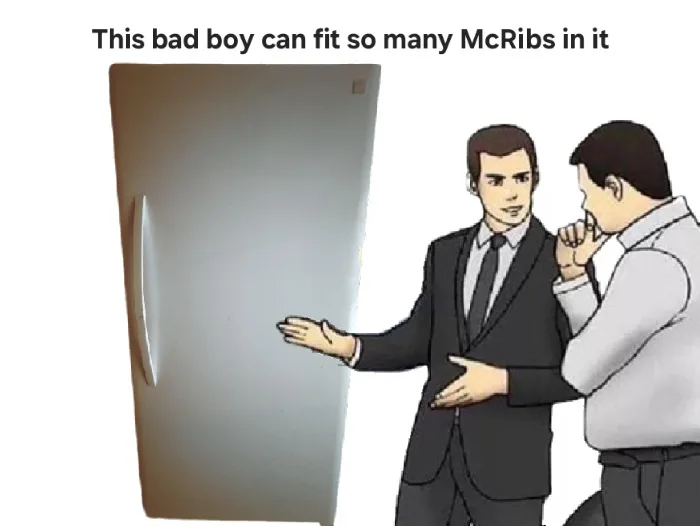 Two men in suits stand beside a large, empty refrigerator. One gestures proudly toward the fridge while the other leans in…