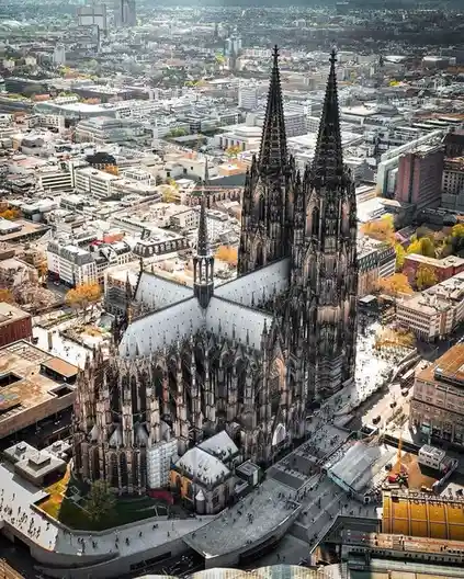 An aerial view of the Cologne Cathedral in Germany, showing its two tall spires and intricate Gothic architecture dominating…