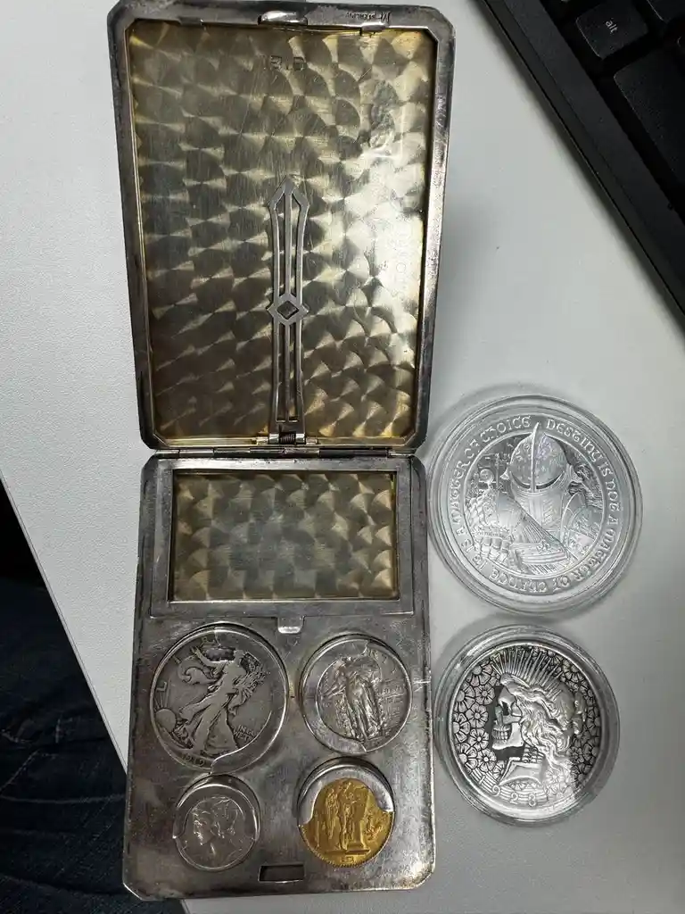 An open, vintage silver cigarette case with a dagger-shaped clasp is displayed on a desk next to a keyboard, holding four…