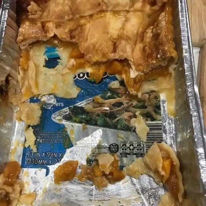 A partially eaten peach cobbler in a foil baking pan reveals the blue and white packaging underneath, which features a…