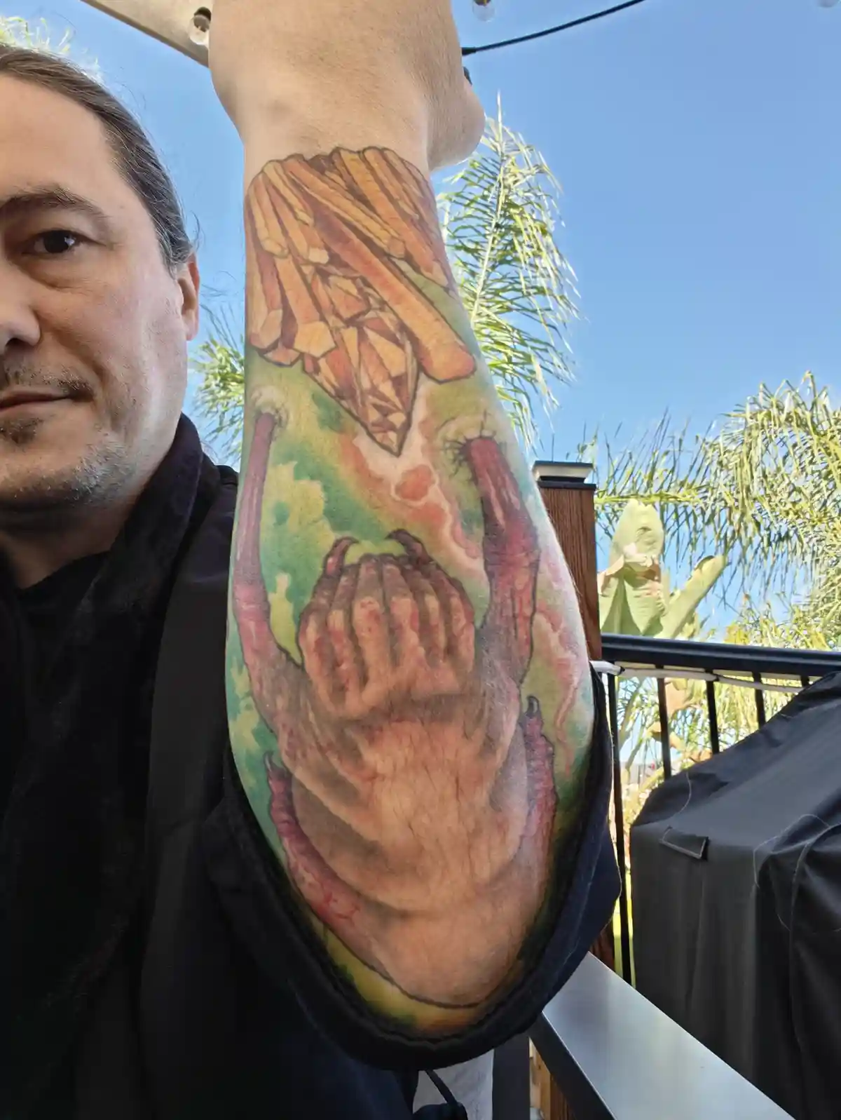 A man holds up his left forearm to display a large, colorful tattoo depicting a hand with red, claw-like fingers gripping a…