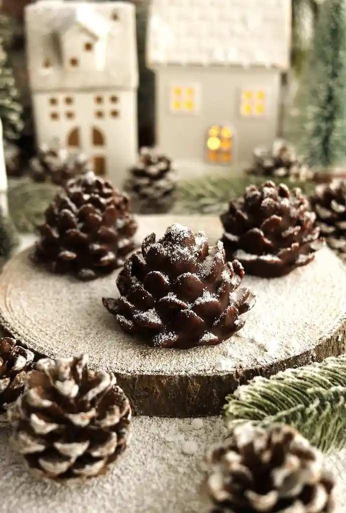 A festive winter scene features several pinecones dusted with artificial snow, arranged on a wooden slice. In the softly…