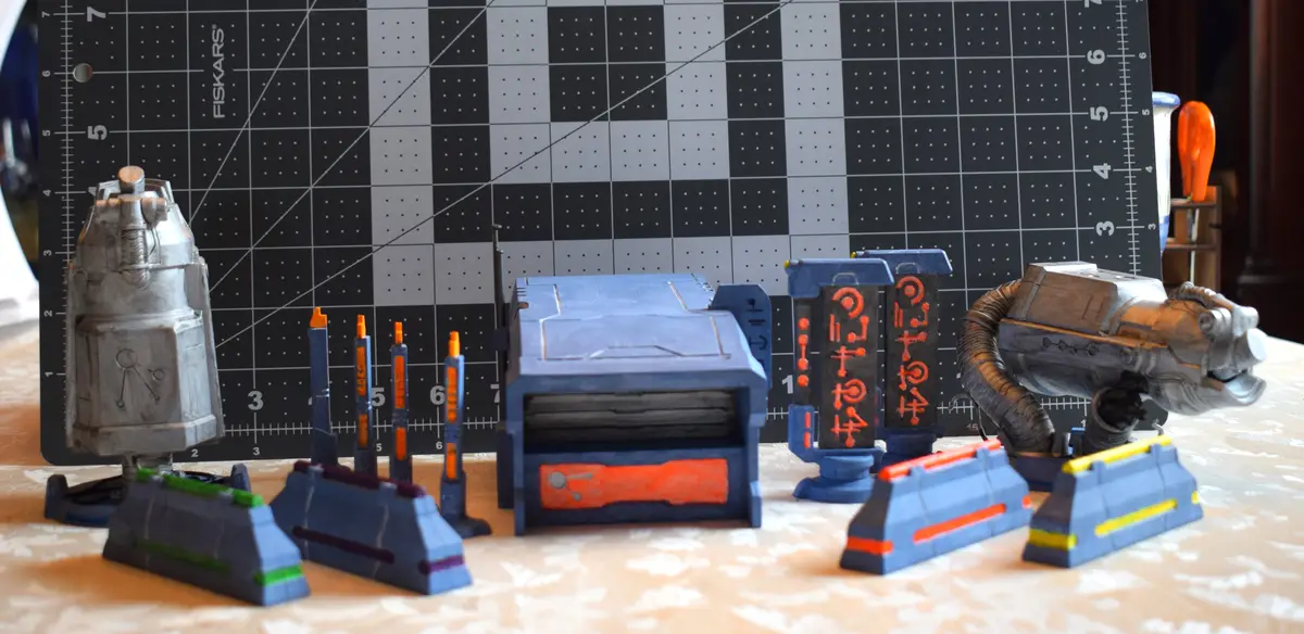 A collection of small, custom-painted science fiction miniatures, including a droid, a box-like structure, pillars with…