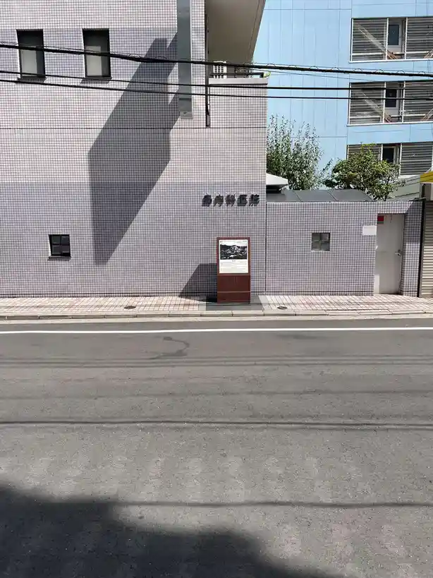 A street view shows a building with a large, dark shadow cast on its tiled wall, shaped like a coffin. The building has…