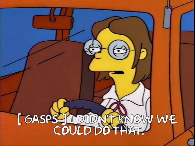 A still from The Simpsons shows a female character with glasses and brown hair, driving a vehicle with a surprised…