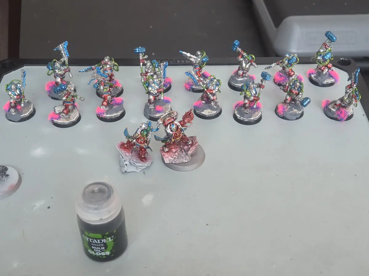 A collection of painted miniature figurines, mostly in red, silver, and blue armor with bright pink fluffy bases, arranged…