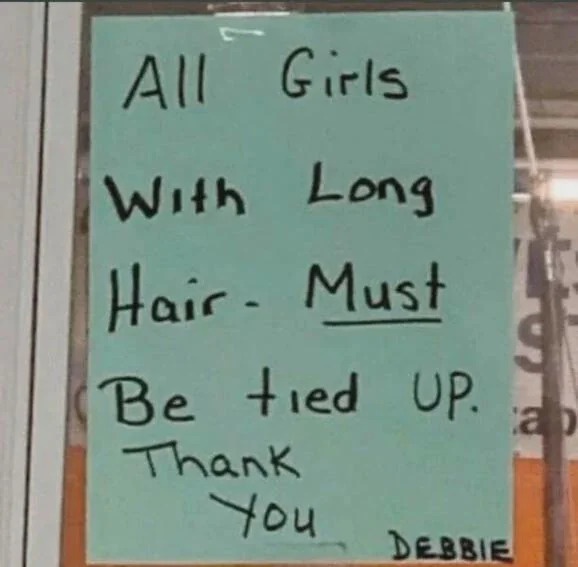 A handwritten note on light blue paper taped to a glass door reads 'All Girls With Long Hair - Must Be tied UP. Thank You'…