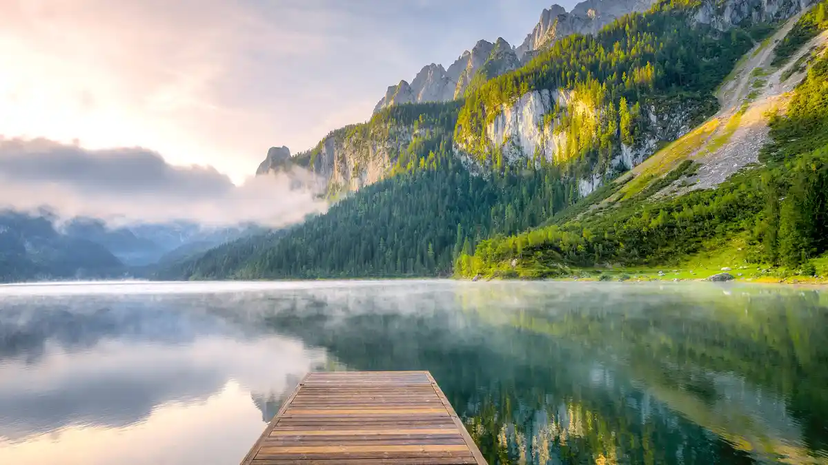 Vorderer Gosausee lake lies serene under a misty summer sunrise. Once a hub for salt production in Austria, locals now enjoy…