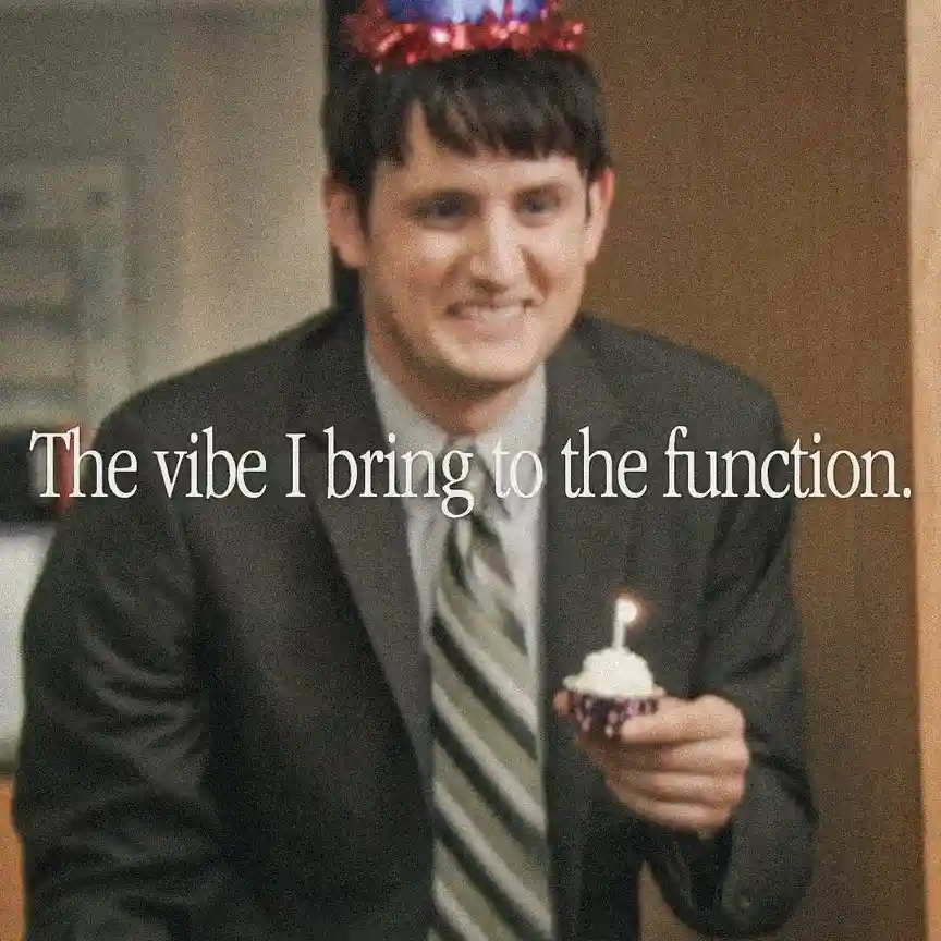 A man in a suit and striped tie wears a red and blue party hat and holds a cupcake with one lit candle. White text overlaid…