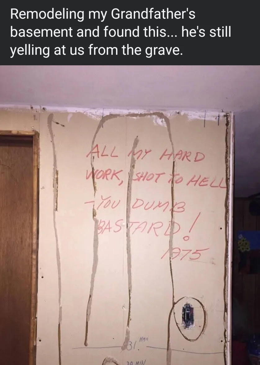 A photo of a partially stripped basement wall with red handwritten text inside a crude outline of a person. The text reads…