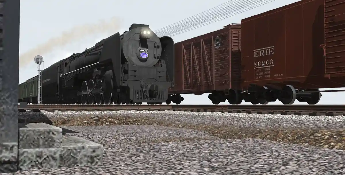A black steam locomotive, numbered 6021, pulls a train with brown boxcars labeled 'ERIE' on tracks. The image has overlaid…