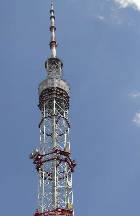 A tall, lattice-style telecommunications tower with red and white sections, multiple satellite dishes, and a spire against a…