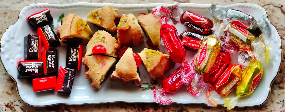A white ceramic tray with a gold rim holds an assortment of Italian confections: on the left, wrapped 'Pocket Coffee'…