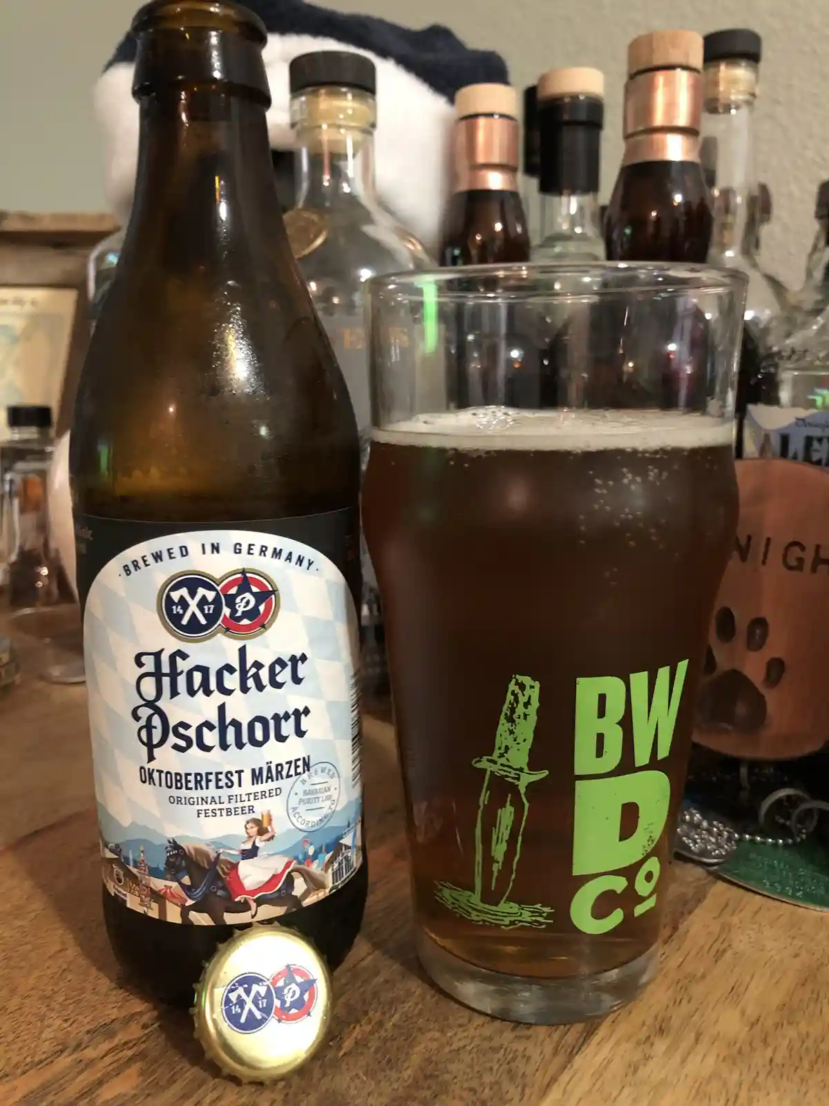 A close-up photo shows a brown bottle of Hacker Pschorr Oktoberfest Märzen beer next to a pint glass filled with dark beer…