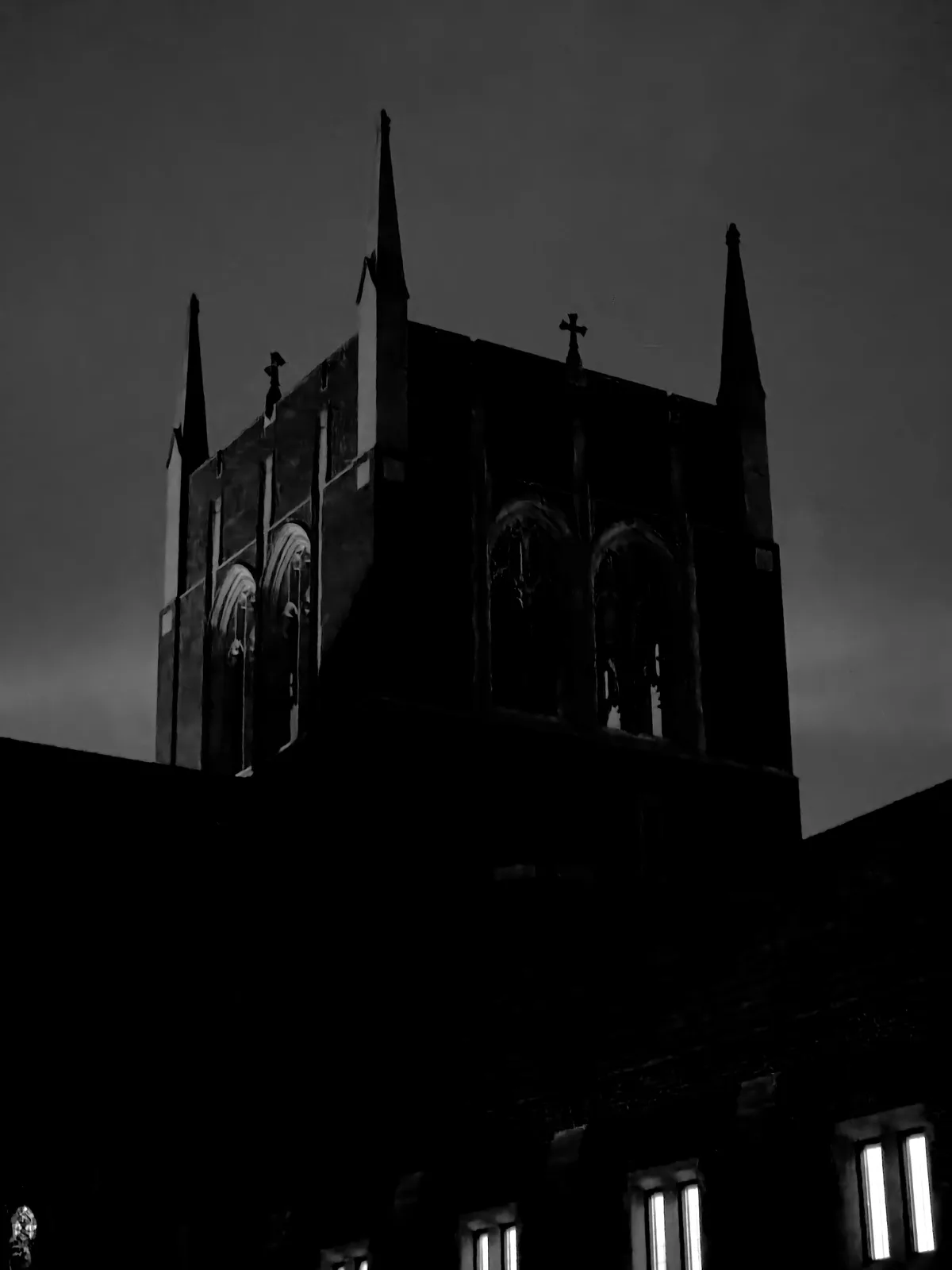 A black and white photo shows the silhouette of a Gothic-style church at night, with pointed spires and arched windows…