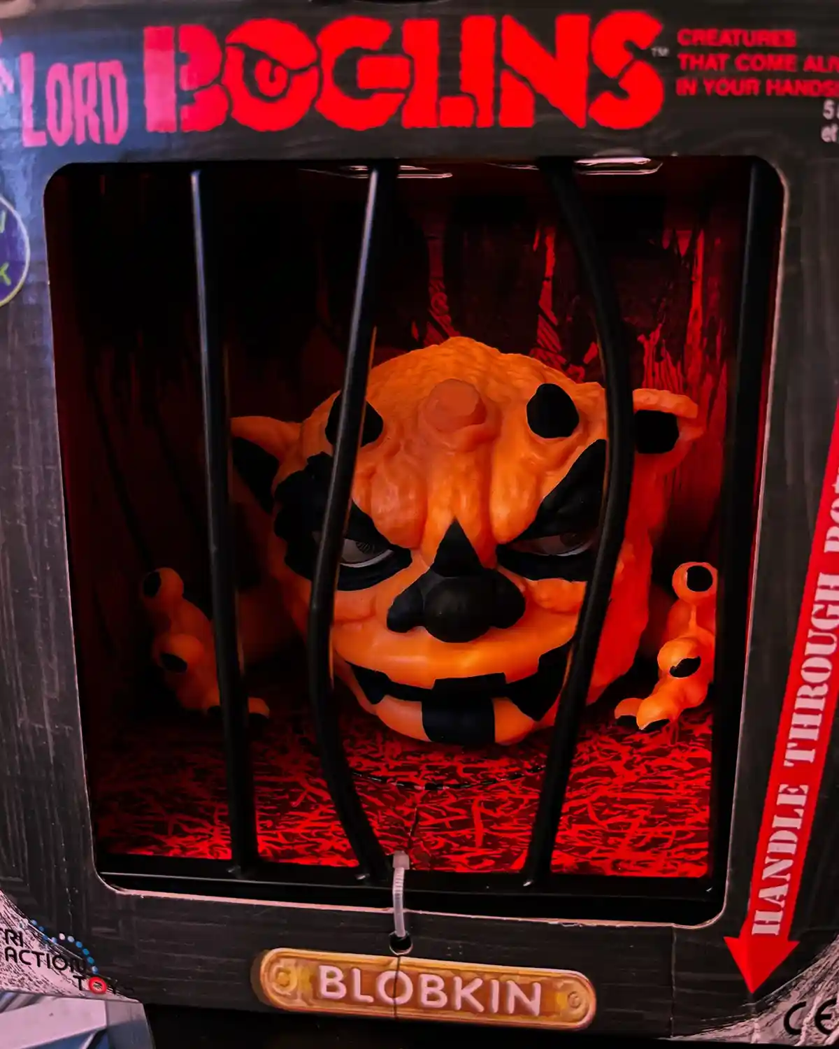 A close-up of a toy called 'Blobkin' from the 'Lord Boglins' series, shown inside its packaging behind black bars. The…