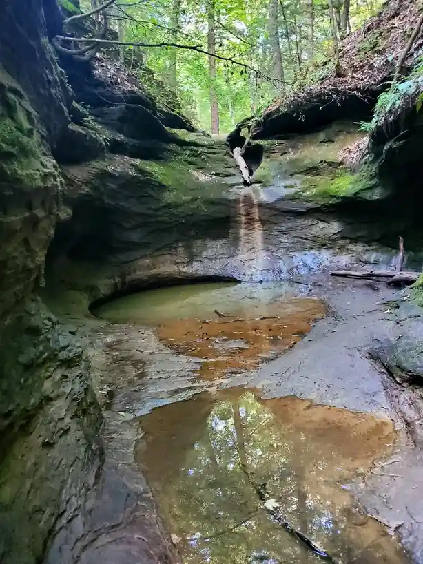 A natural rock formation in a forest with a small waterfall and pools of water, overlaid with the text 'i'm not lazy, i'm in…