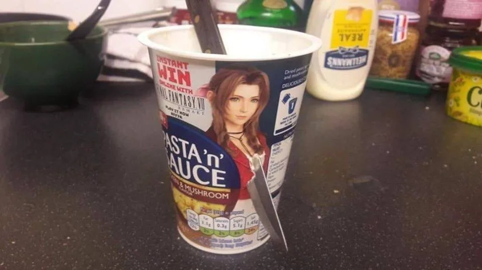 A partially eaten cup of instant pasta and mushroom sauce sits on a kitchen counter with a knife stuck in it. The cup's…