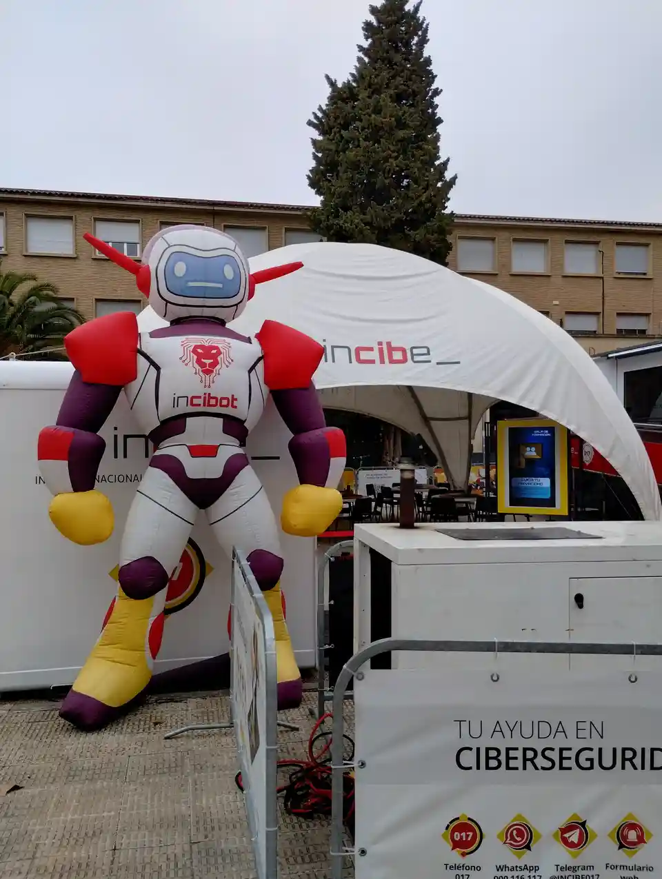 A large inflatable robot mascot named 'incibot' with a red lion logo on its chest stands outside a white tent branded with…