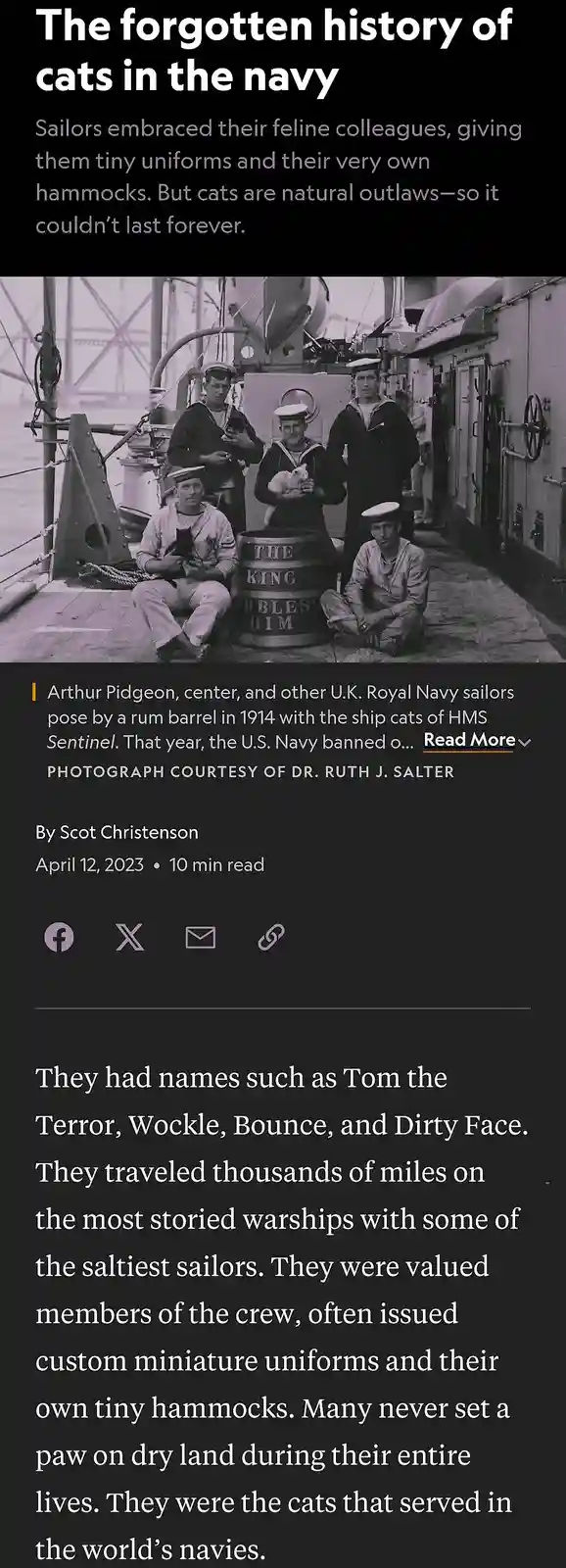 A black-and-white historical photo shows five sailors on a ship deck posing with two cats, one held by a central sailor and…