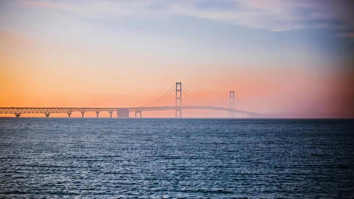 Warm golden hues dance across the horizon as the Mackinac Bridge stretches across the tranquil waters of Lake Huron, its…
