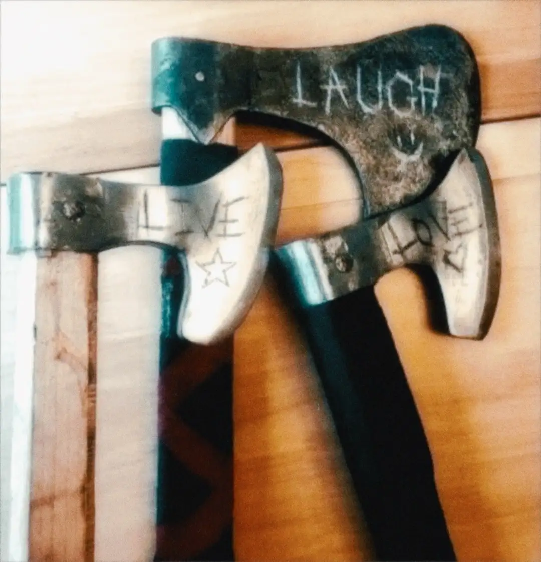 Three axes with handles resting on a wooden surface, each head has words written on it: one says 'LAUGH' with a smiley face…