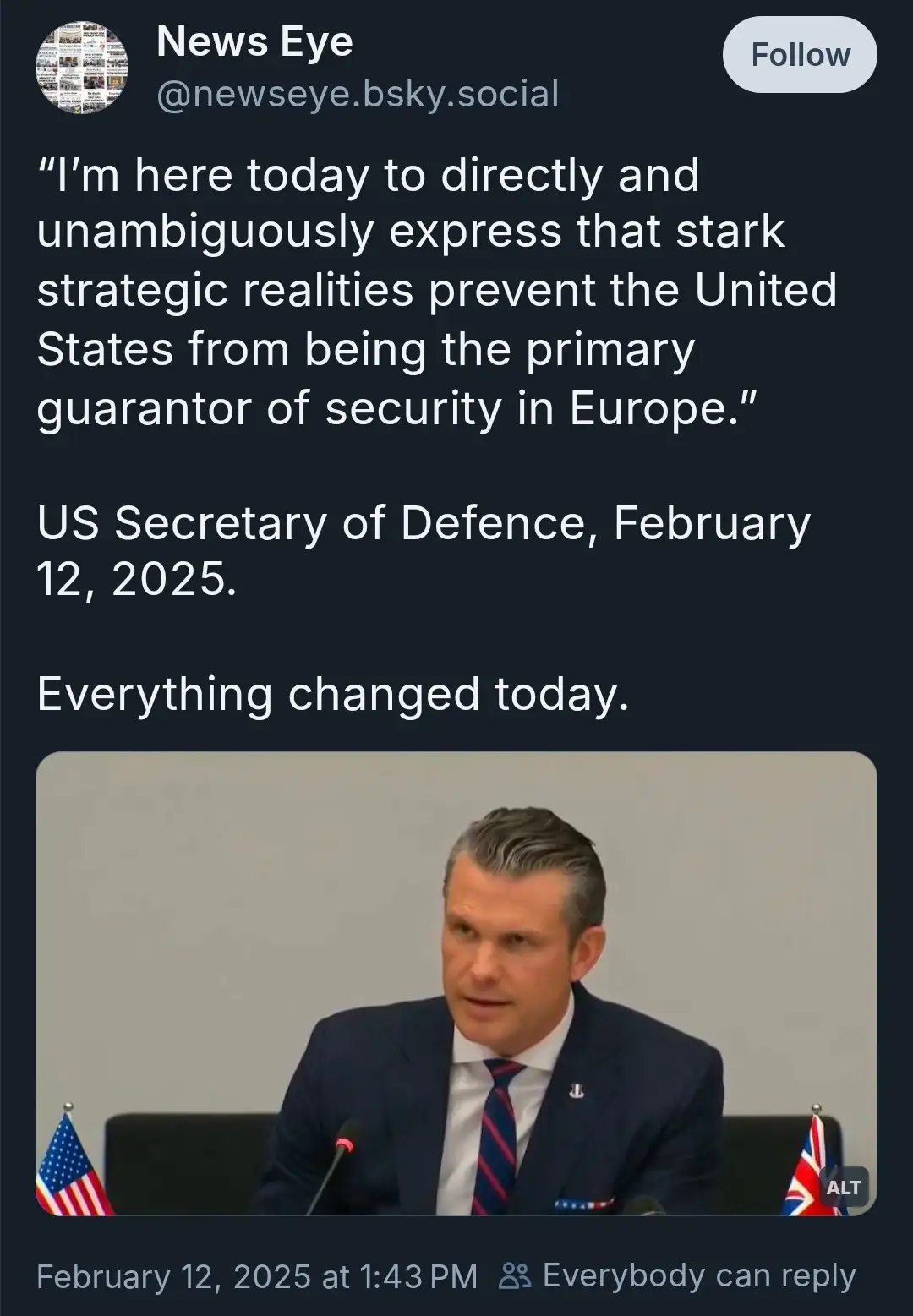 A screenshot of a social media post showing a man in a suit speaking at a podium with American and British flags beside him…