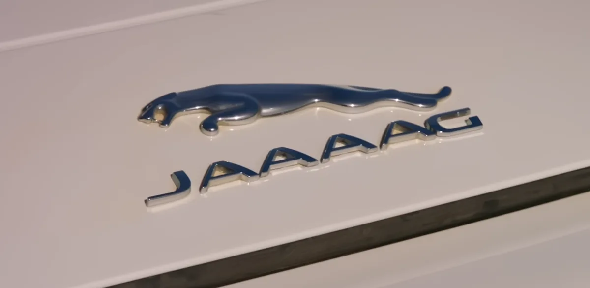 A close-up photo of a Jaguar car emblem, featuring the iconic leaping jaguar logo and the brand name, with the word…