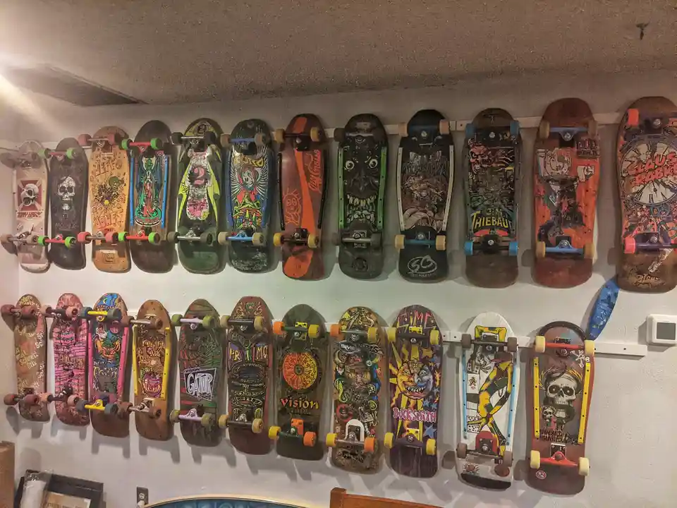 A wall displays two rows of vintage skateboards, each with unique, colorful, and often graphic artwork, mounted…