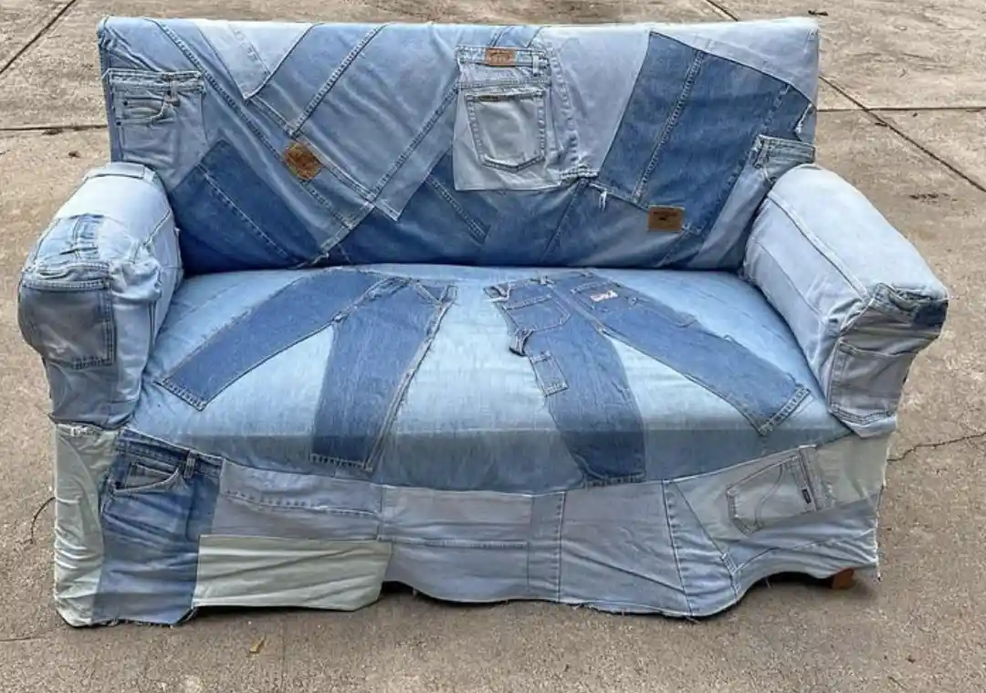 a couch entirely covered in patchwork denim fabric, with visible pockets and seams from various jeans, sitting outdoors on a…