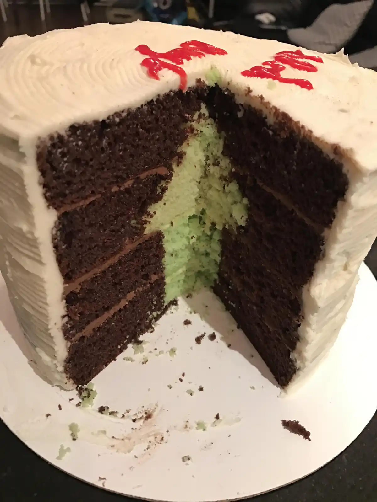 A chocolate cake with white frosting and red 'happy birthday' icing on top has a slice removed, revealing a green cake layer…