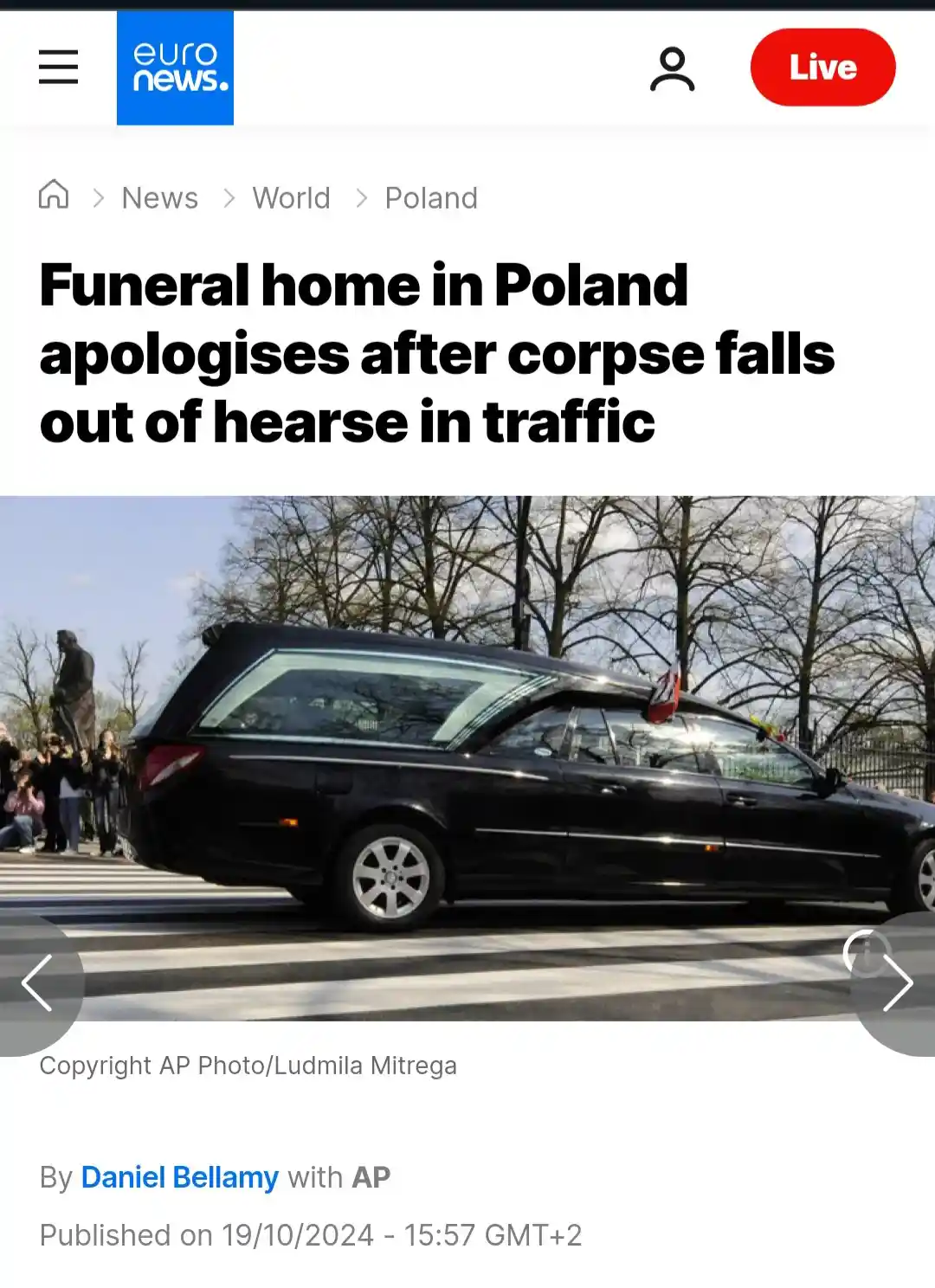 A screenshot of a Euro News article shows a black hearse driving on a street with a crosswalk, with bare trees and a statue…