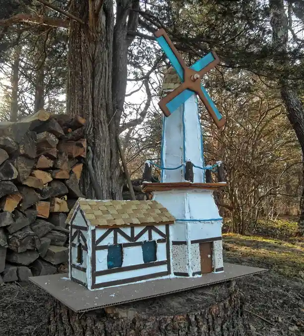 A large, elaborate gingerbread windmill structure, complete with a blue-and-white tower, a thatched roof made of graham…