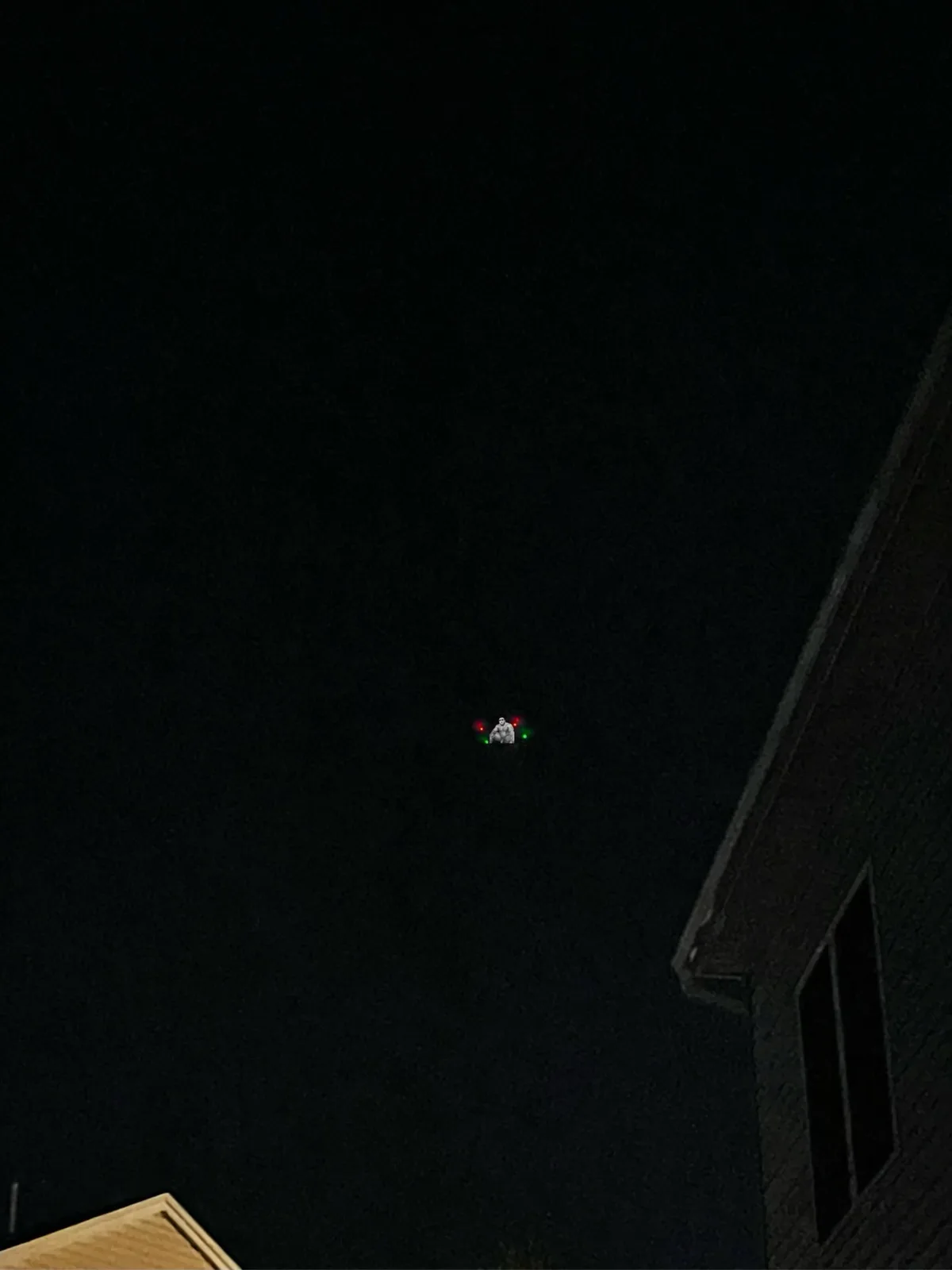 A dark night sky above rooftops features a tiny, distant object with red and green lights, overlaid with an image of a…