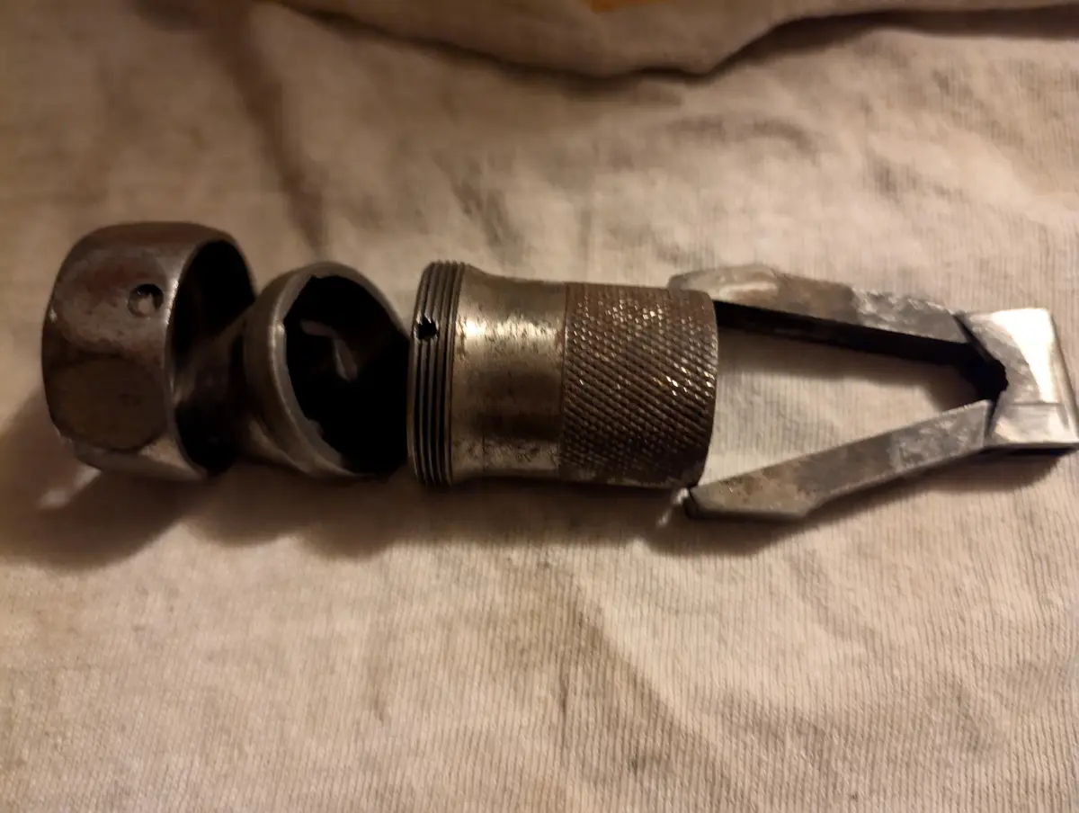 A close-up photo shows a worn, metallic tool with a textured grip and a V-shaped jaw, lying on a light-colored fabric…