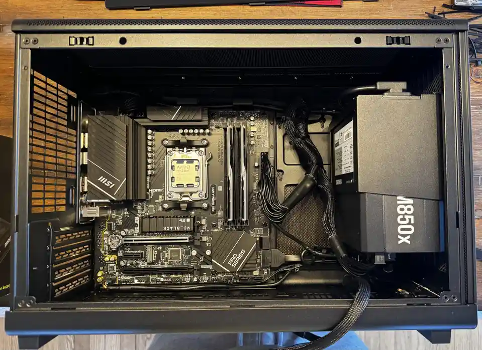 An overhead view of a black computer case with its side panel removed, revealing a motherboard with an AMD Ryzen CPU, MSI…