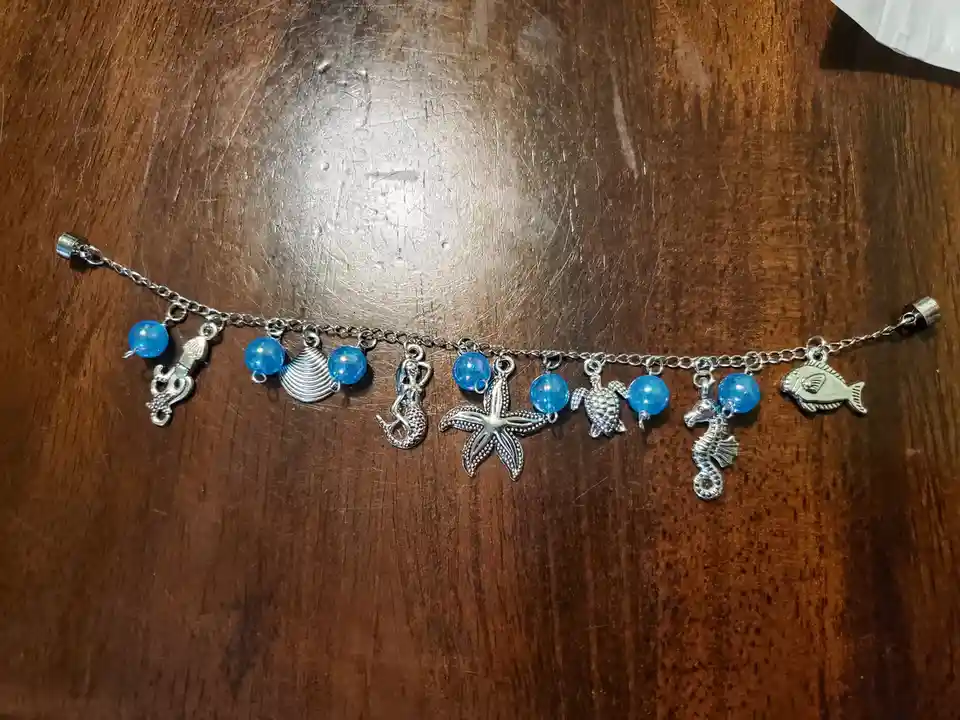 A silver charm bracelet with blue beads and sea-themed charms including a mermaid, starfish, seahorse, turtle, shell, and…