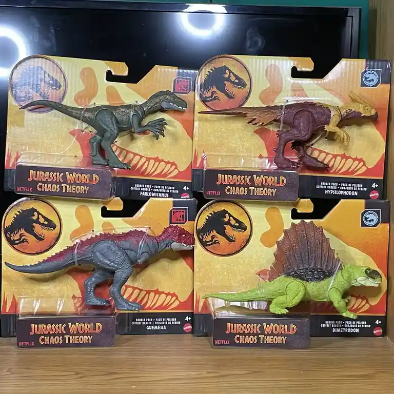 Four Jurassic World Chaos Theory dinosaur action figures in their original packaging are displayed on a wooden shelf. The…
